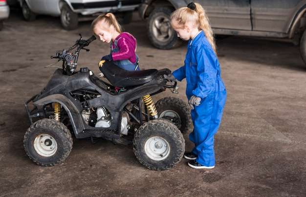 Two little girls in overalls inspecting quad bike 