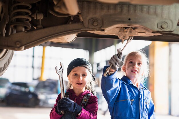 Two little girls in overalls repairing car with spanners 