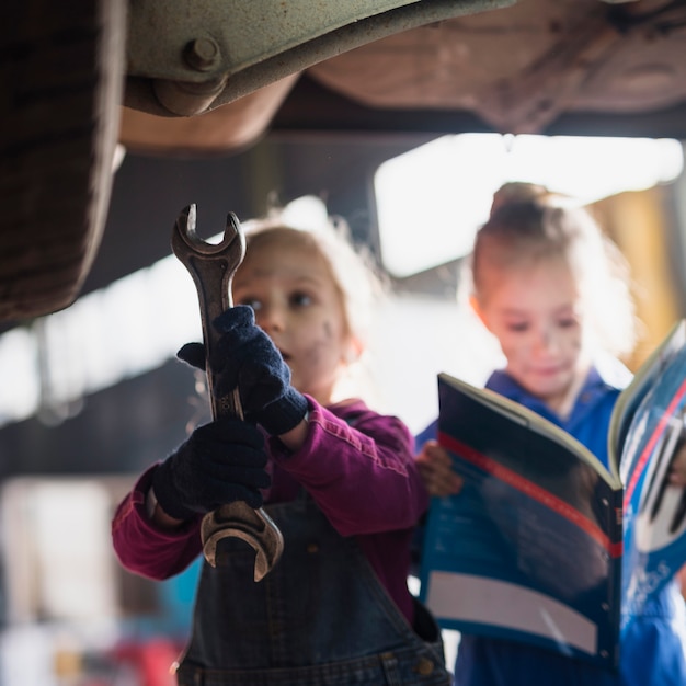 Free photo two little girls in overalls standing with spanner and magazine