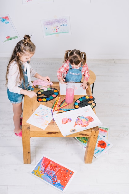 Two little girls painting with aquarelle on paper at table