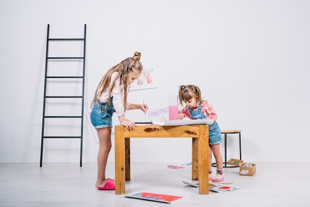 Two little girls painting with aquarelle at table