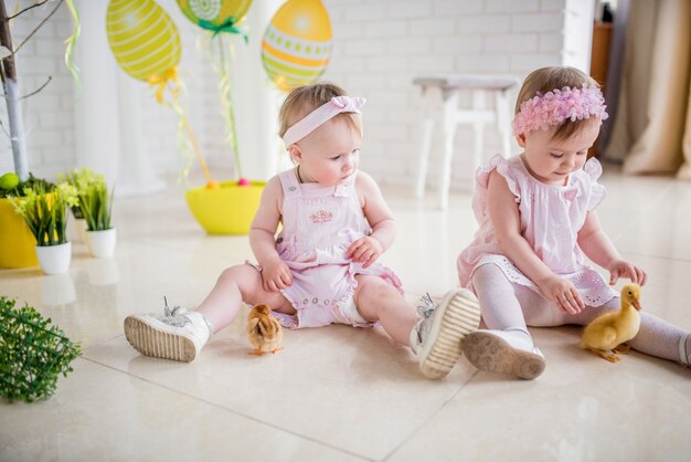 Две маленькие девочки в розовых платьях играют на полу в студии с пасхальным декором