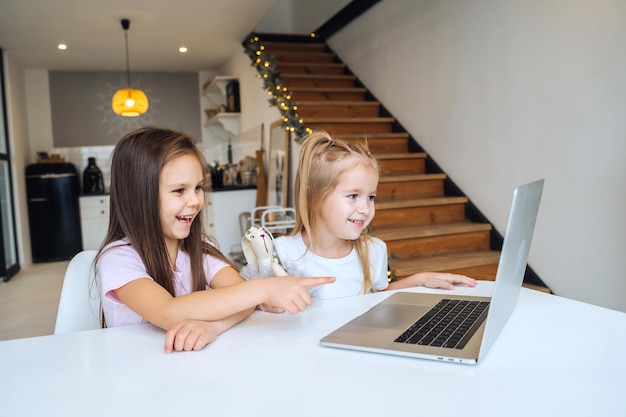 Two little girls playing together at the laptop while sitting at table
