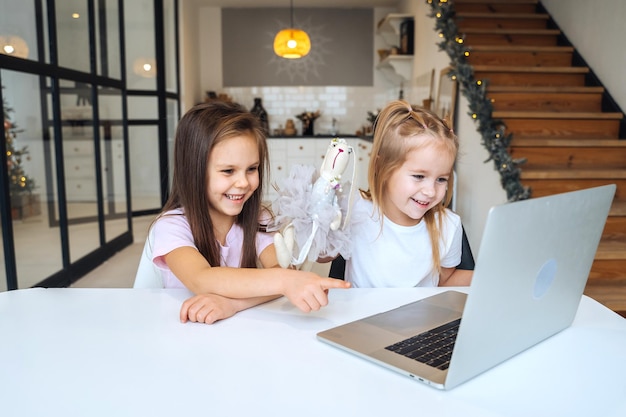 Free photo two little girls playing together at the laptop while sitting at table