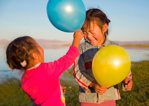 Two little girls playing with each other with balloons.