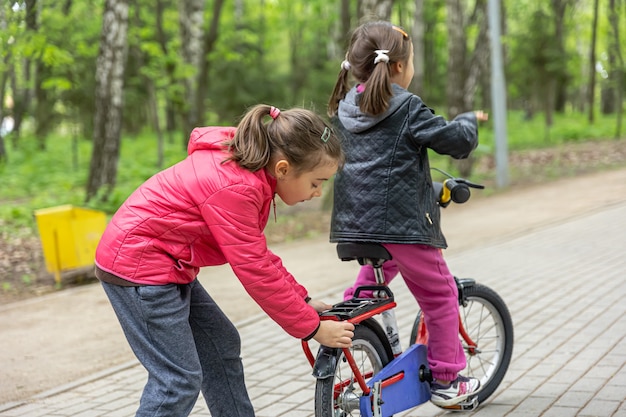 Two little girls ride a bike in the park in spring.