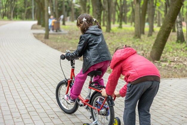 Two little girls ride a bike in the park in spring