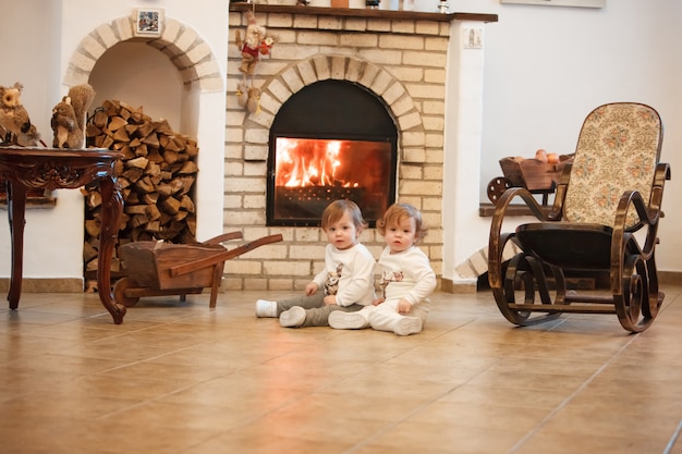 The two little girls sitting at home against fireplace