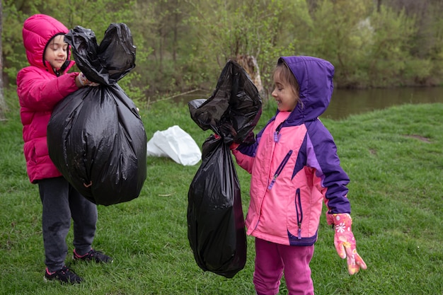 Two little girls with garbage bags on a trip to nature, cleaning the environment