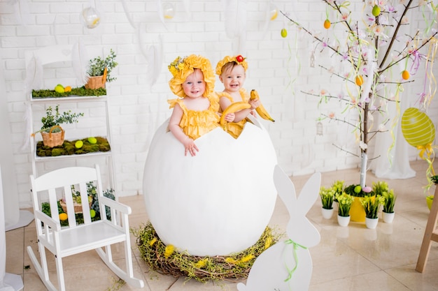 Two little girls in yellow dresses sit in an egg in the studio