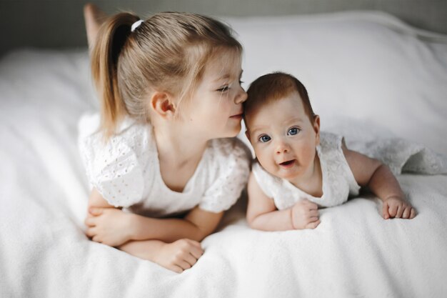 Two little sisters are lying on the bellies, dressed in white cute dresses