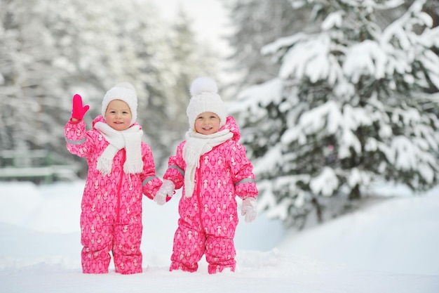 빨간 양복을 입은 두 어린 쌍둥이 소녀가 눈 덮인 겨울 숲에 서 있다