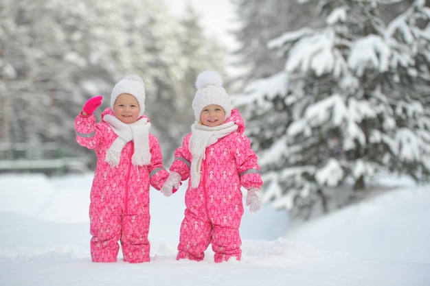 빨간 양복을 입은 두 어린 쌍둥이 소녀가 눈 덮인 겨울 숲에 서 있다