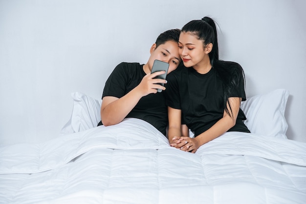 Two loving women sleeping and playing smartphones.