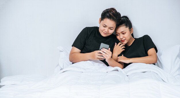 2人の愛する女性が眠り、スマートフォンで遊ぶ。