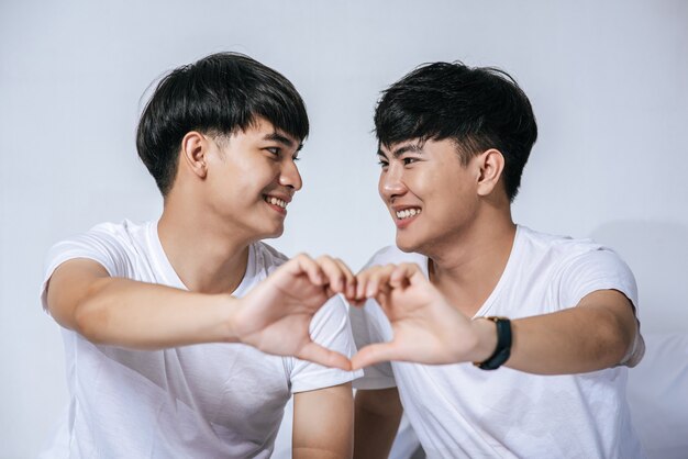 Two loving young men look at each other and make a hand of love symbol.