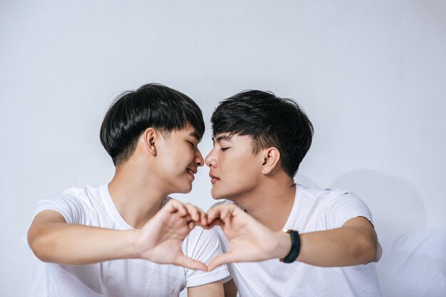 Two loving young men look at each other and make a hand of love symbol.