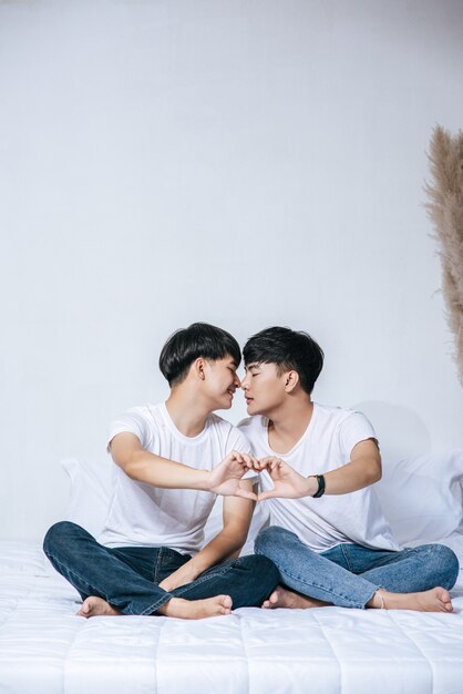 Two loving young men look at each other and make a hand of love symbol.