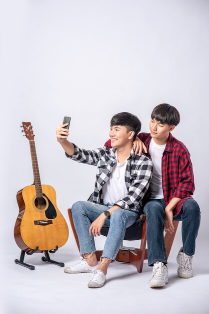 Два любящих юноши сидят на стуле и делают селфи со смартфона.