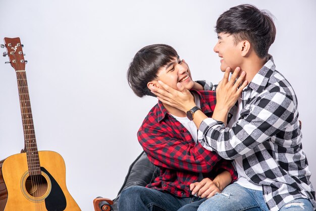 Two loving young men sitting on catch cheek On a chair and with a guitar by the side