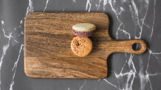 Two macaroons on wooden chopping board over the marble backdrop