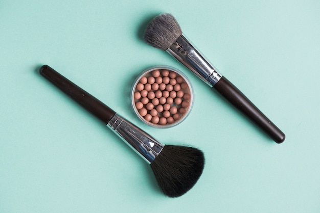 Two makeup brushes with bronzed pearls over green background