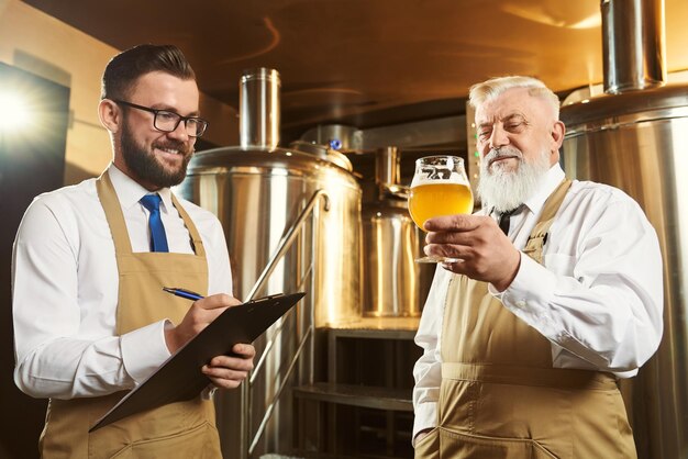 Two male brewery workers examining beer