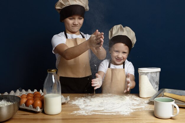 Two male children preparing dough while backin biscuit or cookies for their mother on her birthday. Cute happy little boys posing in modern kitchen interior with hands in flour, cooking bread