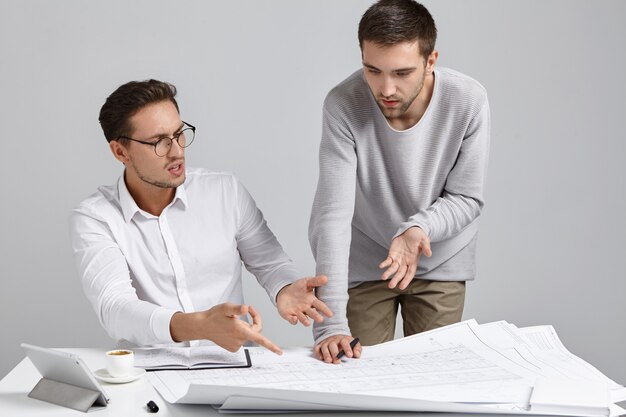 Two male colleagues architects having argument concerning architectural plan, expressing their points of view