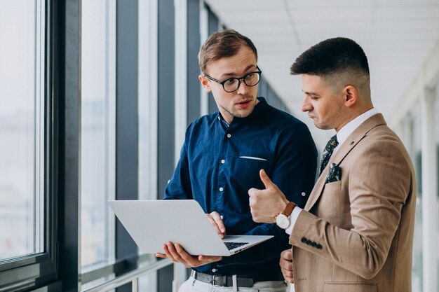 Two male colleagues at the office,standing with laptop