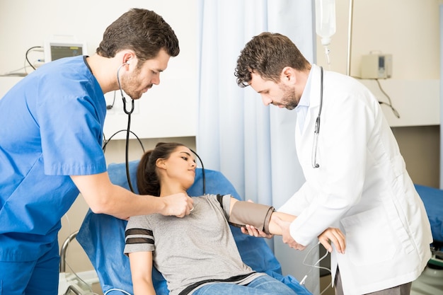 Two male doctors checking heart beats and blood pressure of a female patient in emergency room