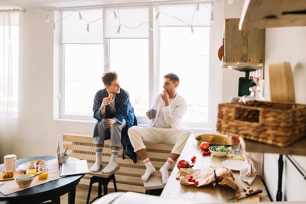 Two male friend sitting in kitchen eating breakfast