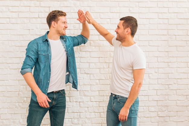 Two male friends giving high five to each other against white brick wall