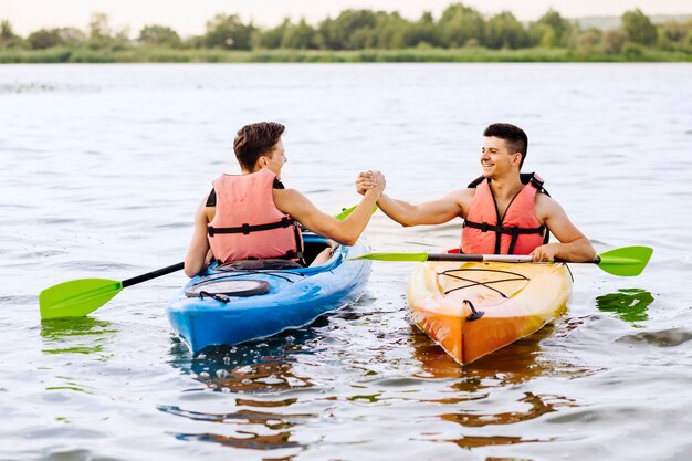 Two male friends shaking each other's hand while kayaking on lake