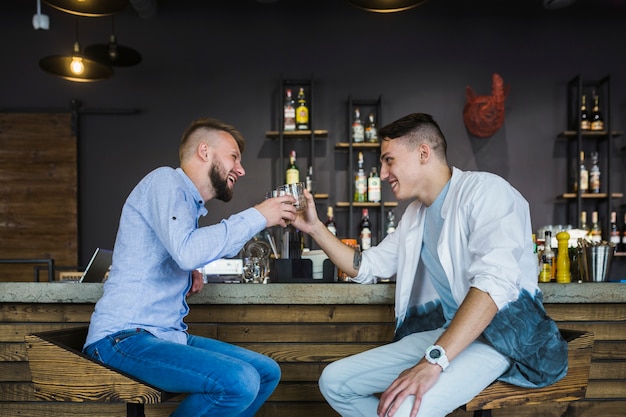 Two male friends sitting at bar counter toasting glasses of drinks