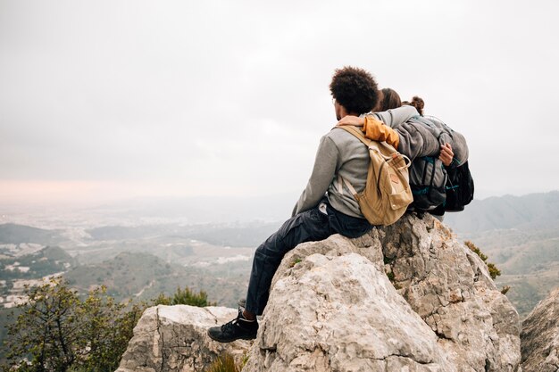 Два мужчины турист, сидя на вершине скалы над горой, глядя на живописный вид