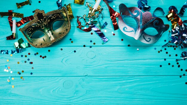 Карнавальная маска с двумя маскарадами и праздничными украшениями над синим деревянным столом