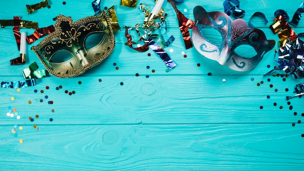 Карнавальная маска с двумя маскарадами и праздничными украшениями над синим деревянным столом