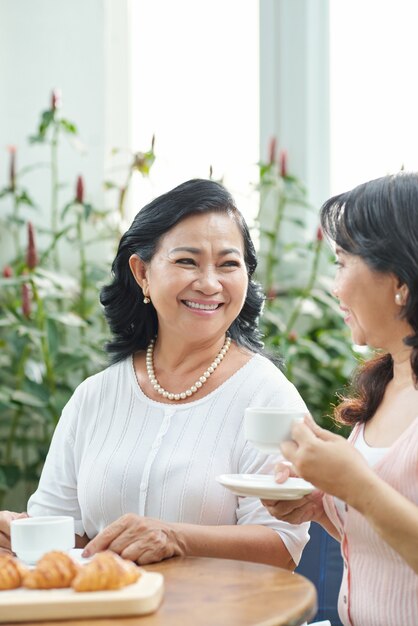 Two mature Asian ladies enjoying coffee with croissants in cafe