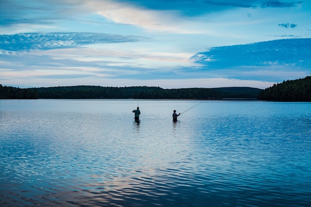 Two men fishing in a calm lake under the blue sky