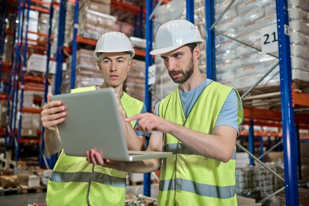 倉庫で仕事の質問を決定するラップトップを見ている2人の男性
