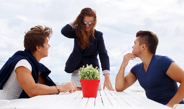 Two men at the table and redhead woman against cloudy sky.