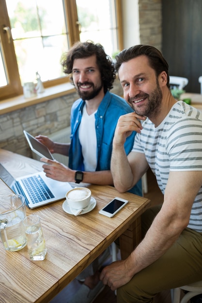 Free photo two men using digital tablet and laptop at coffee shop