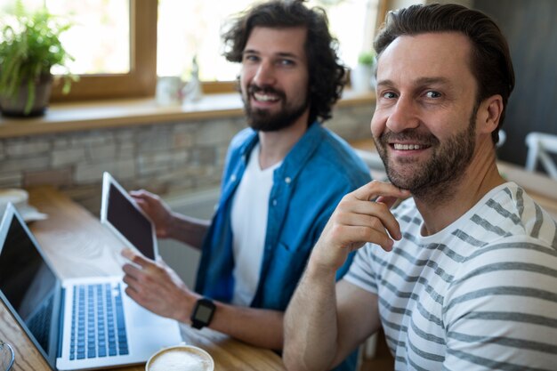 Two men using digital tablet and laptop at coffee shop