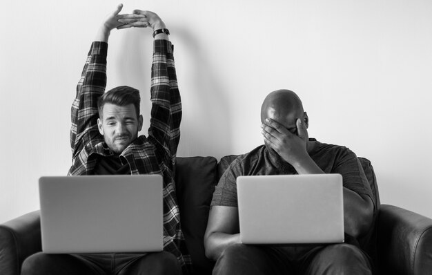 Two men using laptop sitting on sofa