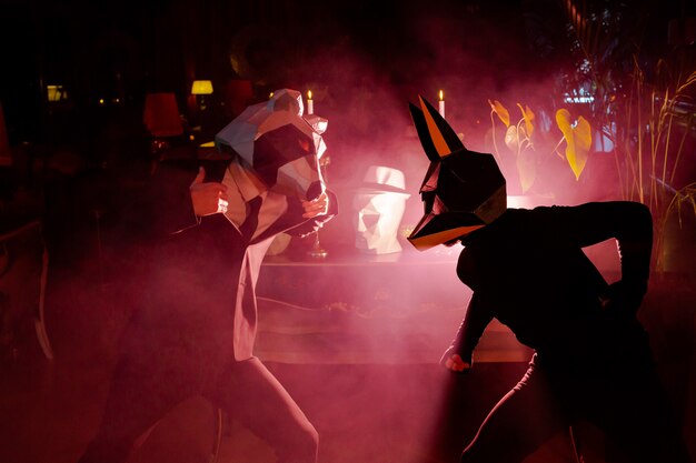 Two men wearing animal masks at the party in the club with red lights