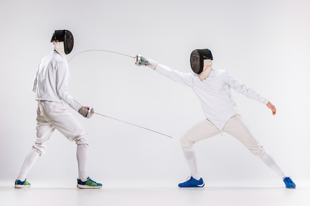 The two men wearing fencing suit practicing with sword against gray