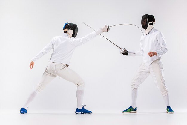 Free photo the two men wearing fencing suit practicing with sword against gray