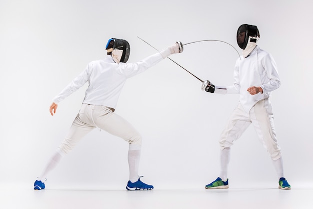灰色に対して剣で練習フェンシングスーツを着ている2人の男性