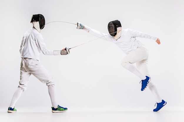 灰色に対して剣で練習フェンシングスーツを着ている2人の男性